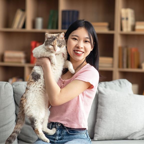 A woman holds up her cat while sitting on a couch
